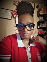 Dr. Yolanda wearing a red shirt, with hoop earrings, and glasses with her hair up in a bun.
